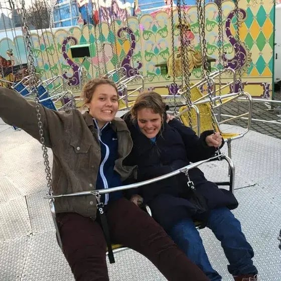 Zwei Menschen sitzen in einem Kettenkarussell. Eine Person winkt